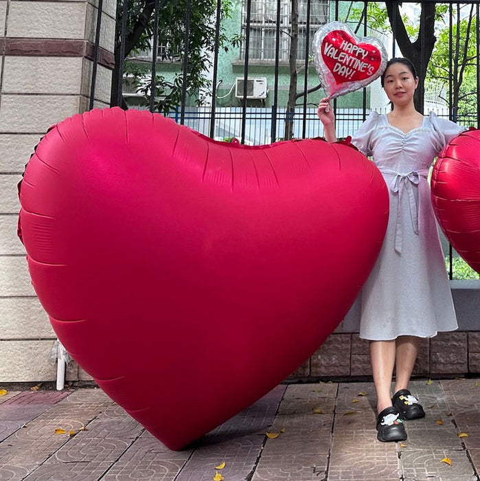 A 68-inch Valentine's Day GIANT Heart Shaped Mylar Balloon. Balloon is shown with a persona and a standard mylar balloon for scale.